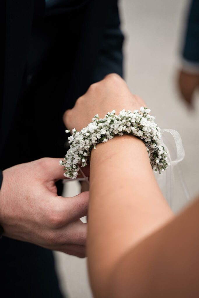 Braut bekommt ein Blumenband um ihr Handgelenk angelegt, Detailaufnahme.