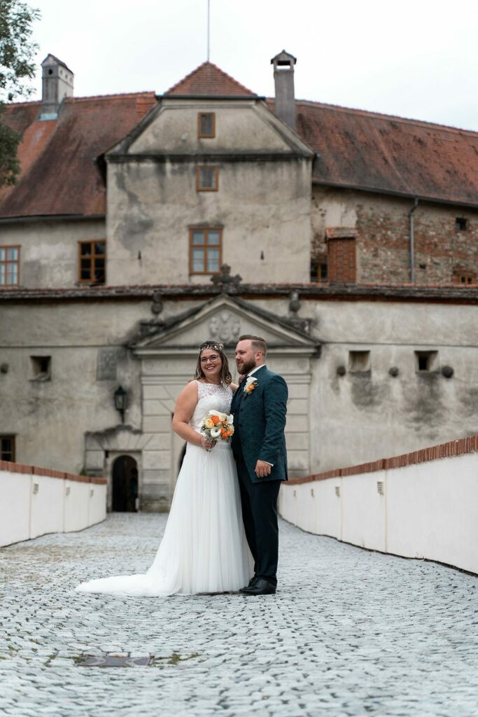 Vor der majestätischen Burg steht das Brautpaar in Hochzeitsgarderobe.