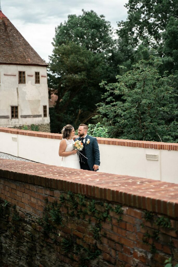 Hochzeitsfoto auf der Brücke, von weiter weg mit der Burg und Wald im Hintergrund.