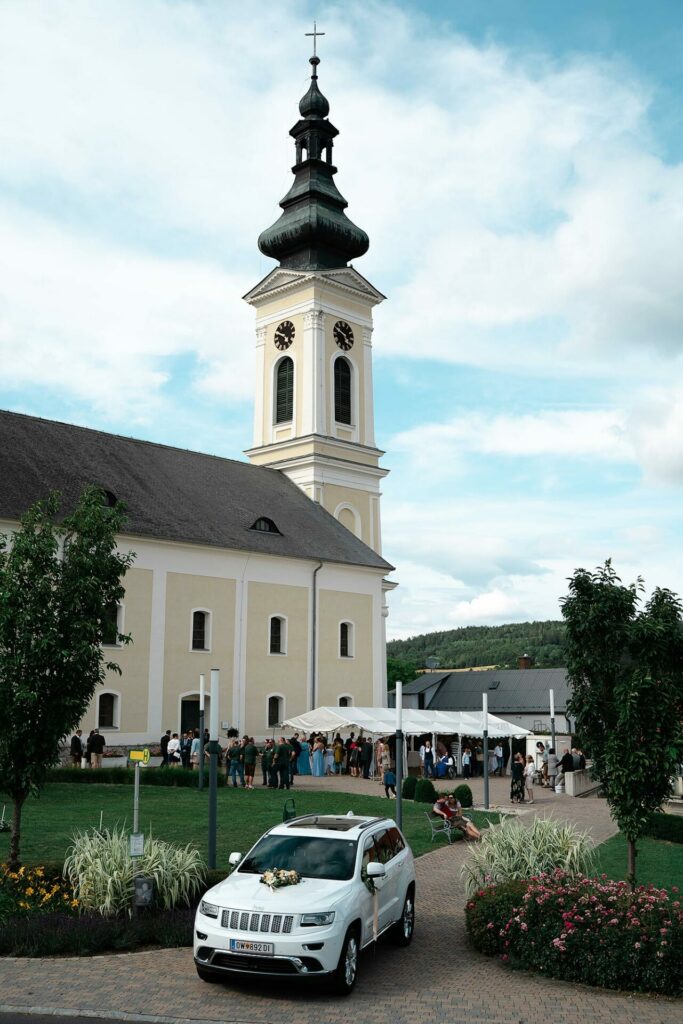 Die Kirche in Stadtschlaining, mit den Gästen der Hochzeit und dem dekorierten Auto.