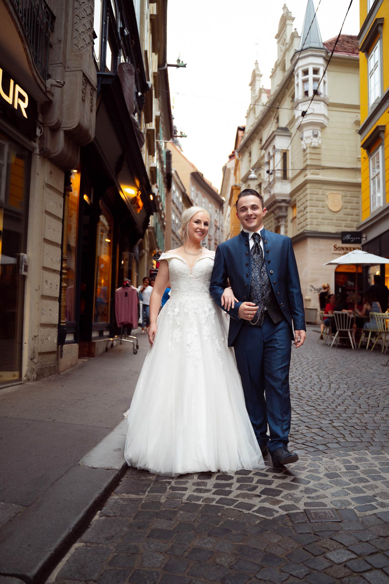 Brautpaar beim After Wedding Shooting am Fuße der Grazer Sporgasse. Die beiden spazieren Hand in Hand und lächeln in die Kamera.