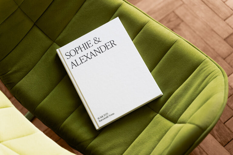 Hochzeitsbildband mit weißem Hardcover mit Leineneinband auf einem grünen Stuhl